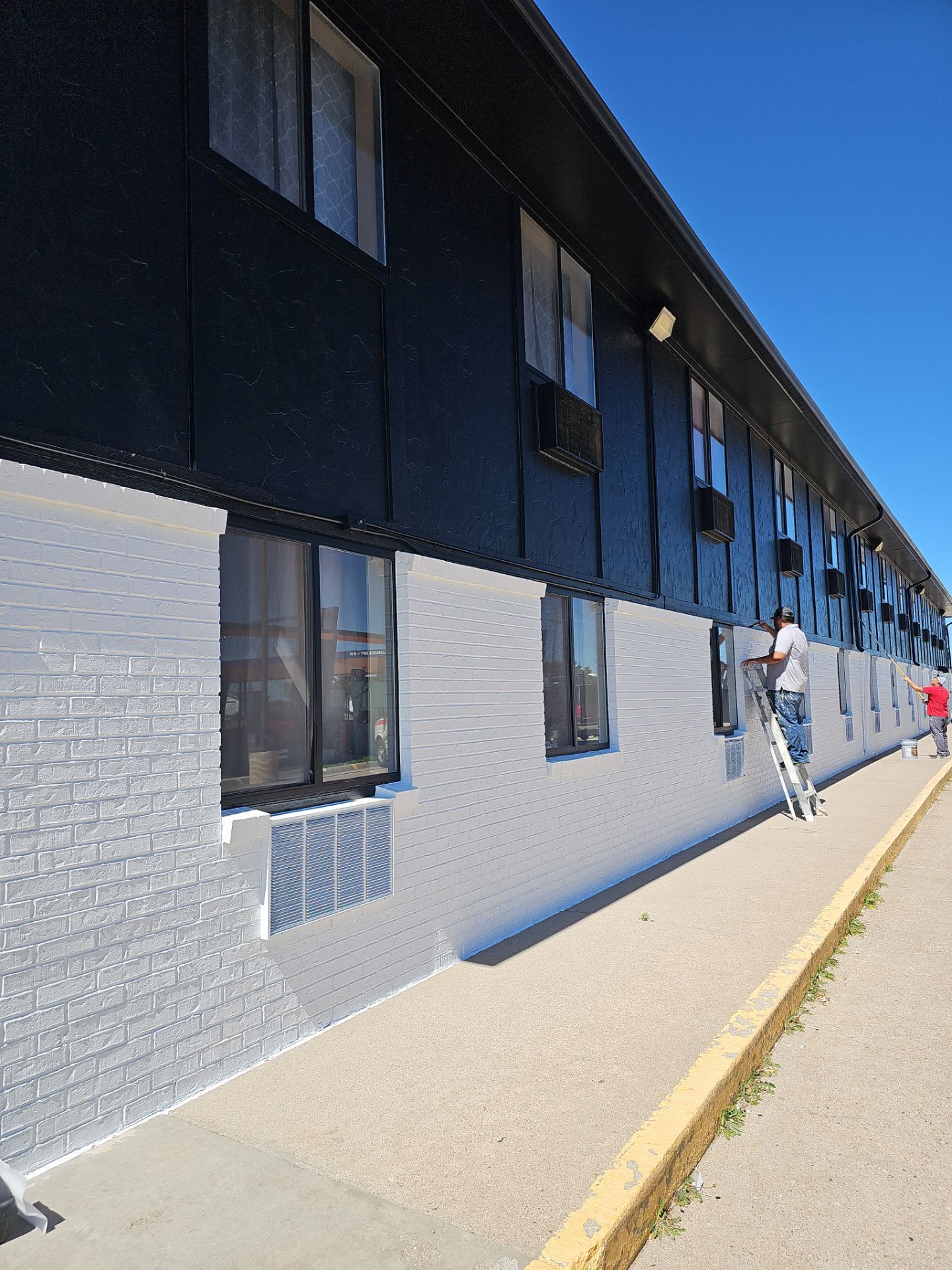 Painter on a ladder cutting in black window trim on a commercial property