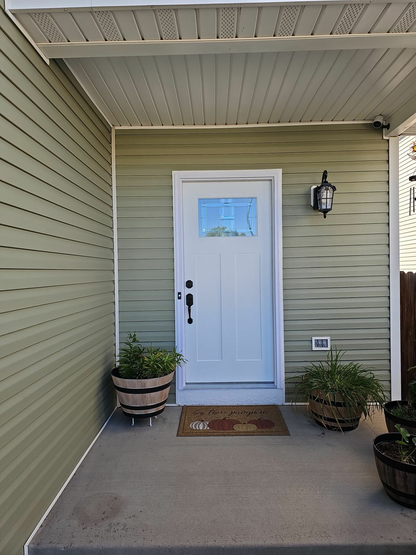 Covered porch entry with sage green siding, white door, and painted soffits