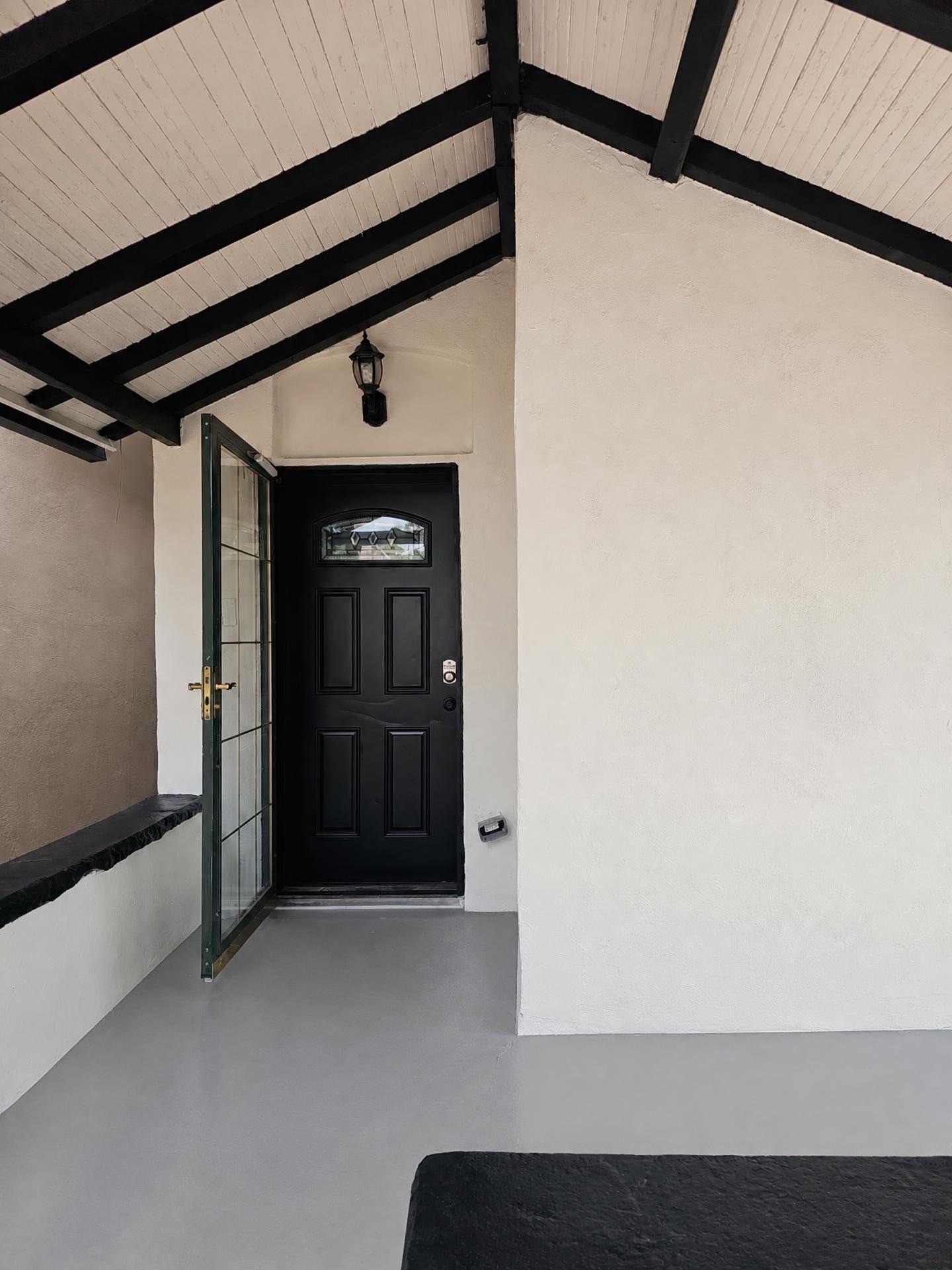 Stucco entryway painted warm cream with black timber beams and door